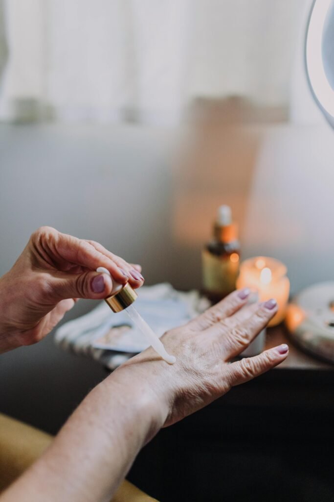 Close-up image of a hand applying skin care serum using a dropper. Indoor setting with warm lighting.