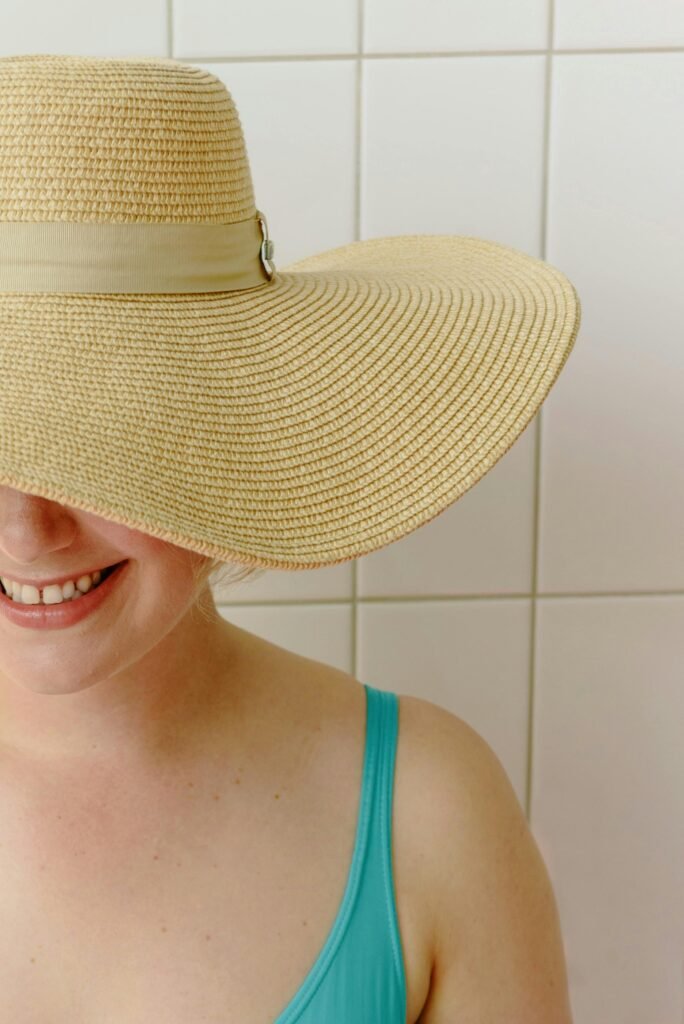 A cheerful woman wearing a wide-brimmed sun hat, partially hiding her face, with a bright smile.