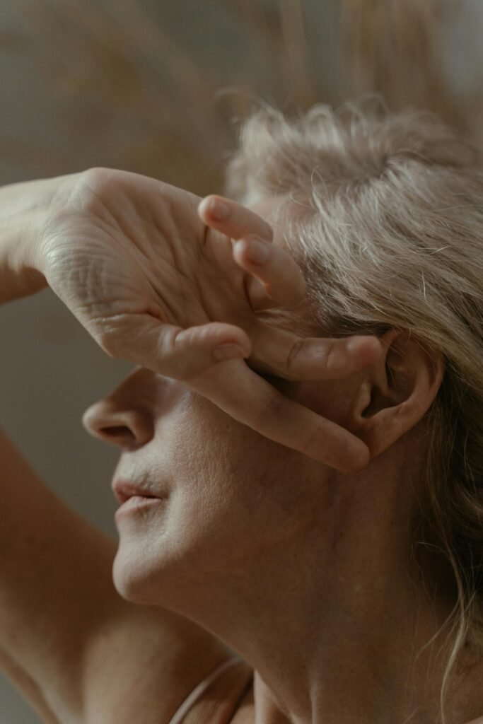 An intimate portrait of an elderly woman with her hand gently covering her face, captured in soft, muted tones.